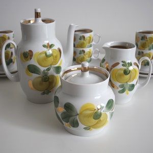 Könnte beinhalten: Ein weißes Porzellan-Tee-Set mit gelbem und grünem Blumendesign. Das Set enthält eine Teekanne, eine Zuckerdose, eine Milchkännchen und vier Tassen und Untertassen.