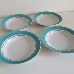May include: Four white oval-shaped bowls with a turquoise border and a gold accent line. The bowls are arranged on a white surface, showcasing a clean and minimalist aesthetic. These bowls are suitable for serving soups or salads.
