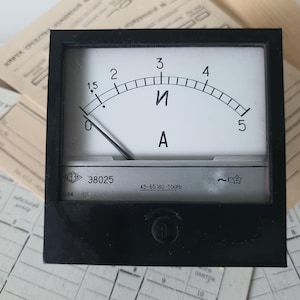 Può includere: Un amperometro analogico nero con quadrante bianco, con scala curva da 0 a 5, contrassegnata dalla lettera "A". L'ago punta vicino allo zero. Il misuratore riporta le scritte "И" e "38025".