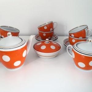Puede incluir: Un juego de té blanco con lunares naranja y blanco. El juego incluye una tetera, un azucarero, una jarra de crema y cuatro tazas de té y platillos.