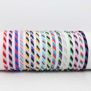 Peut inclure: Un ensemble de 16 bracelets d'amitié colorés avec une variété de motifs rayés. Les bracelets sont faits de ficelle tissée et mesurent environ 18 cm de long.