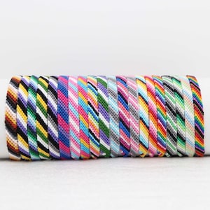 May include: A stack of colorful friendship bracelets with various striped patterns. The bracelets are made of woven string and are a popular accessory for both men and women.
