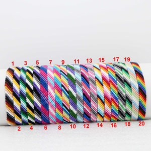 Può includere: Venti braccialetti dell'amicizia colorati con diversi motivi a righe. I braccialetti sono numerati da 1 a 20.