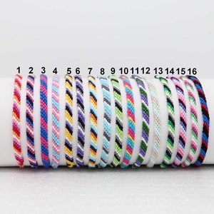 Peut inclure: Seize bracelets d'amitié colorés avec différents motifs rayés. Les bracelets sont numérotés de 1 à 16.