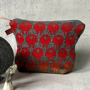 Könnte beinhalten: Eine graue Garnspule und ein kleiner Beutel mit Reißverschluss. Der Beutel hat ein sich wiederholendes rotes Blumenmuster auf grauem Hintergrund. Eine kleine Keramikfigur ist ebenfalls vorhanden.