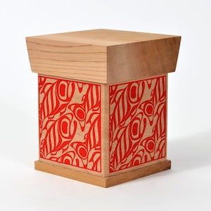 May include: A wooden box with a red and white geometric design. The box has a hinged lid and is made of light wood.