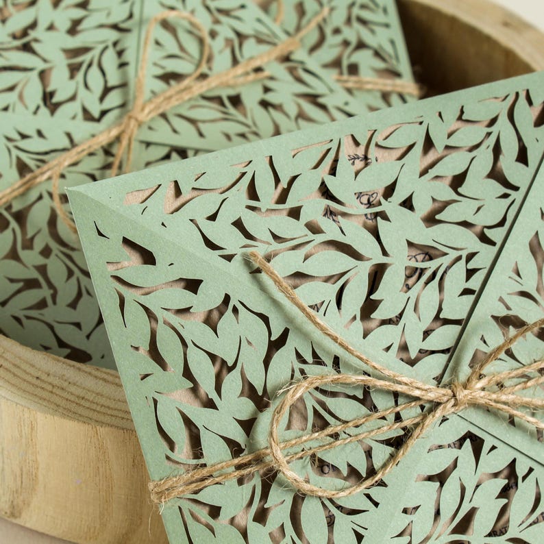 Peut inclure: Enveloppes en papier d&eacute;coup&eacute;es au laser de couleur verte avec un motif feuillu d&eacute;licat, attach&eacute;es avec de la ficelle. Les enveloppes sont empil&eacute;es les unes sur les autres.