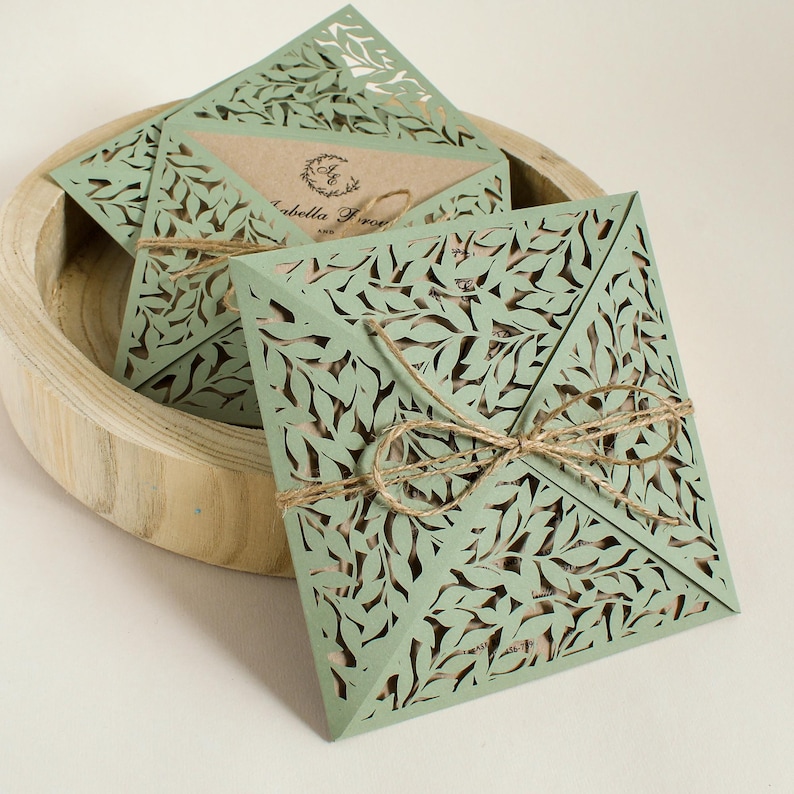 Peut inclure: Enveloppes en papier d&eacute;coup&eacute;es au laser de couleur verte avec un motif de feuilles. Les enveloppes sont attach&eacute;es avec de la ficelle et ont une insertion en papier brun.