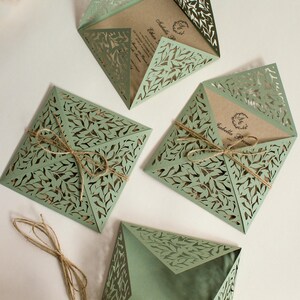 Peut inclure: Quatre invitations de mariage d&eacute;coup&eacute;es au laser de couleur verte avec un motif de feuilles. Les invitations sont pli&eacute;es et attach&eacute;es avec de la ficelle.