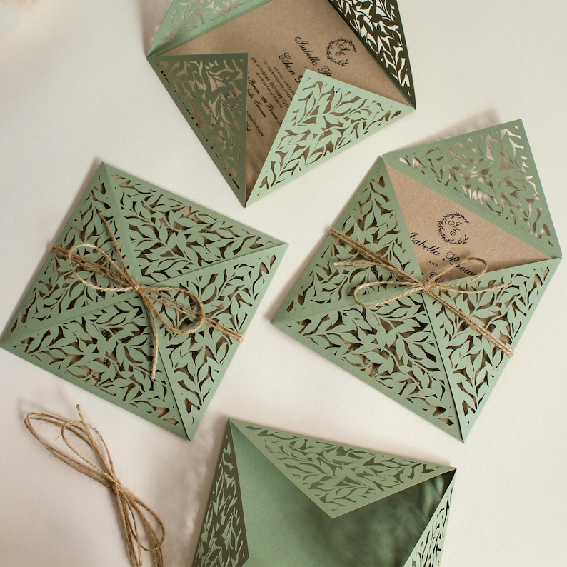 Peut inclure: Quatre invitations de mariage d&eacute;coup&eacute;es au laser de couleur verte avec un motif de feuilles. Les invitations sont pli&eacute;es et attach&eacute;es avec de la ficelle.