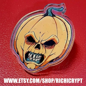 May include: A clear acrylic pin featuring a cartoon pumpkin with a skull face. The pumpkin is orange with a green stem and the skull is white with black eyes and a toothy grin. The pin is a Halloween themed decoration.