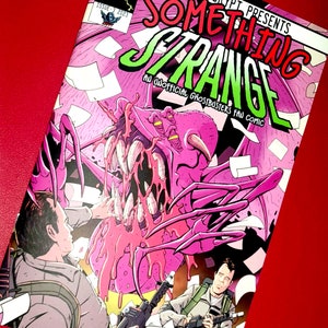Puede incluir: Una portada de cómic con un monstruo rosa con dientes afilados y múltiples ojos. El título del cómic es "Something Strange: An Unofficial Ghostbusters Fan Comic".