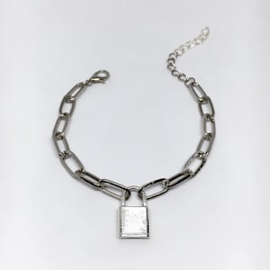 May include: Silver-toned chain bracelet with a rectangular padlock charm. The bracelet features a series of elongated oval links connected by smaller links. The padlock charm hangs from the center of the bracelet.