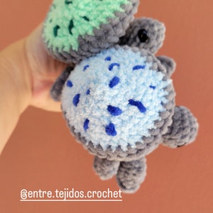 May include: A crocheted turtle toy with a green shell and a blue and gray spotted body. The toy is held in a hand and the text '@entre.tejidos.crochet' is visible below the toy.