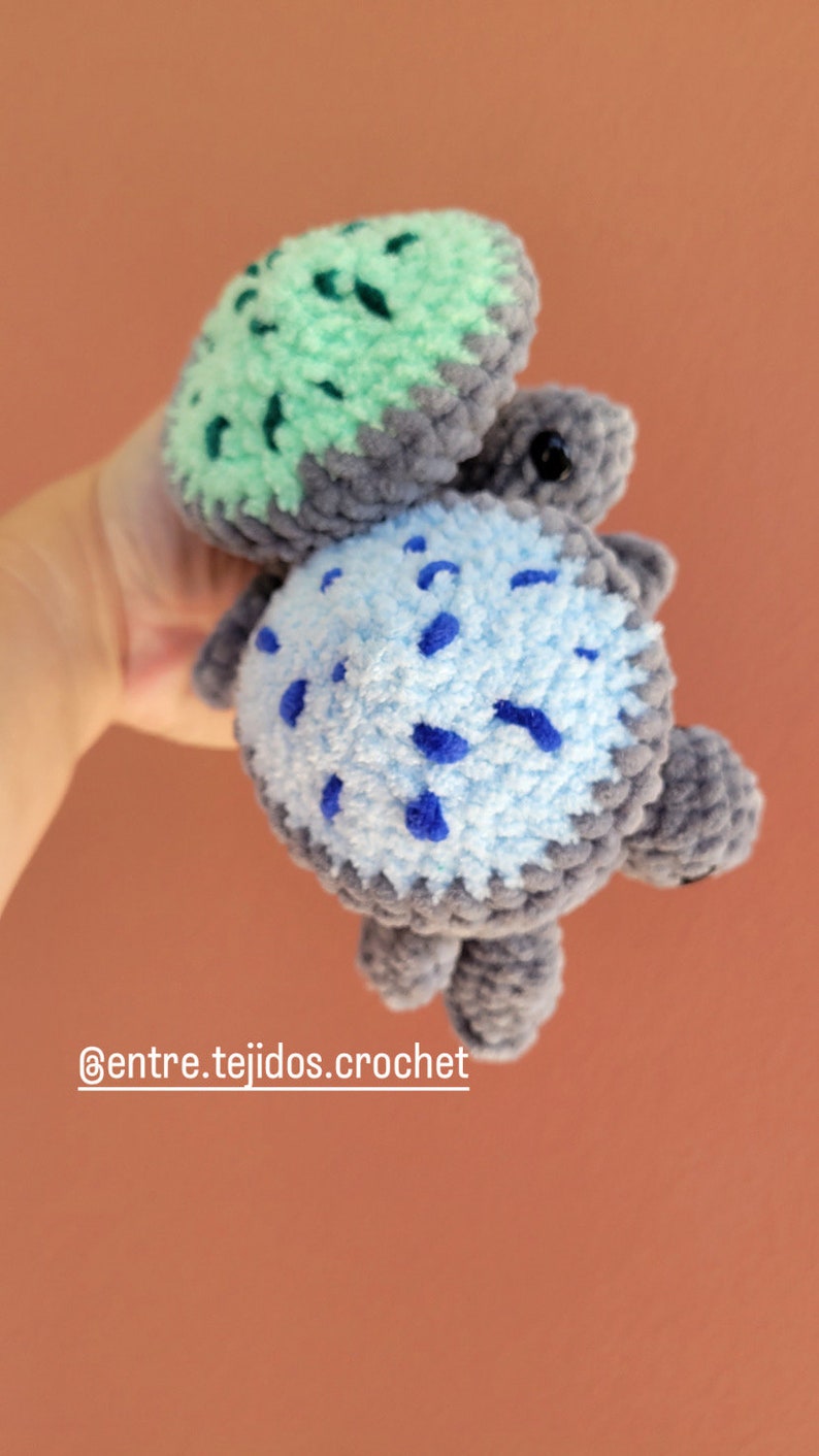 May include: A crocheted turtle toy with a green shell and a blue and gray spotted body. The toy is held in a hand and the text '@entre.tejidos.crochet' is visible below the toy.