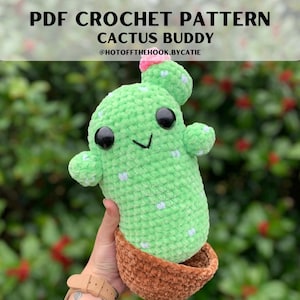 May include: A crocheted cactus plushie with a smiling face, black eyes, and a pink flower. The cactus is light green with white spots and sits in a brown pot. Text on top reads "PDF CROCHET PATTERN CACTUS BUDDY".