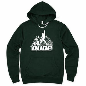May include: Dark green hoodie with a white graphic featuring a mountain scene, a Bigfoot-like figure, and the text "Mountain Dude." The hoodie has a drawstring hood and a front pocket.