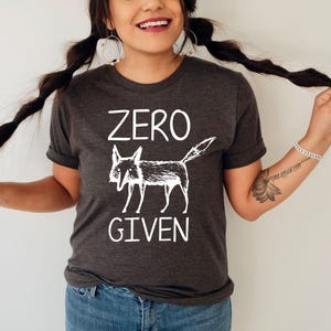 May include: Dark gray t-shirt with a white graphic of a fox and the words "ZERO GIVEN". The shirt has short sleeves and a crew neck. The design features a stylized fox illustration.