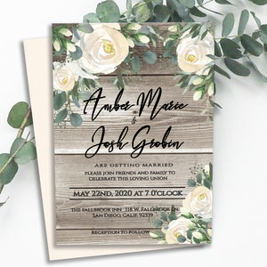 May include: Rustic wedding invitation with white flowers and greenery on a wood background. The invitation reads "Amber Marie & Josh Grobin are getting married. Please join friends and family to celebrate this loving union. May 22nd, 2020 at 7 o'clock. The Fallbrook Inn, 118 W. Fallbrook Inn, San Diego, Calif. 92339. Reception to follow."