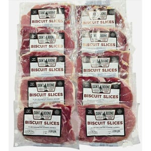 May include: An overhead shot of multiple packages of Dan'l Boone Country Ham Biscuit Slices. The packages are clear, showing the pinkish-red ham slices. Each package has a black and white label with the brand name and product description.