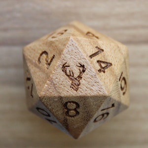 Puede incluir: Un dado de madera de 16 caras con los números del 1 al 16 y un diseño de cabeza de ciervo en una cara.