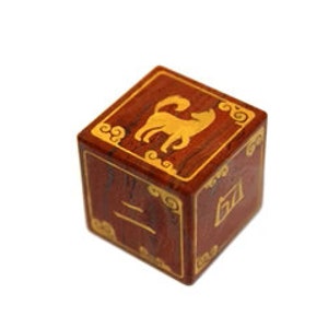 May include: A wooden cube with a gold dog symbol and Chinese characters on each side. The cube is a dark reddish brown color.