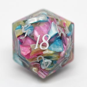 Könnte beinhalten: Ein mehrfarbiger, irisierender D20-Würfel aus Harz mit der weißen Zahl 18 auf einer Seite. Der Würfel ist mit kleinen, bunten, irisierenden Materialstücken gefüllt.