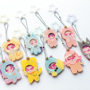 Peut inclure: Une collection de porte-clés en acrylique représentant des personnages de dessins animés en costumes d'animaux. Chaque porte-clés est doté d'une chaîne argentée et d'un fermoir en forme d'étoile. Les personnages sont de différentes couleurs, dont le jaune, le bleu, le rose et le gris.