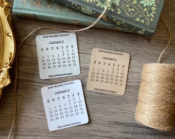 May include: Three white cards with black text, each showing a January 2026 calendar. The cards are on a wooden surface with a roll of twine.