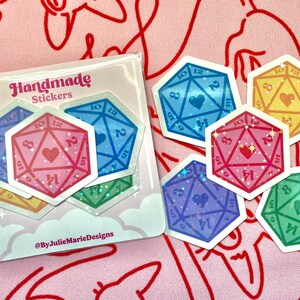 Pode incluir: Um conjunto de seis adesivos feitos &agrave; m&atilde;o com dados coloridos e brilhantes com cora&ccedil;&otilde;es no centro. Os adesivos est&atilde;o em um fundo branco com o texto "Handmade Stickers" e "@ByJulieMarieDesigns".