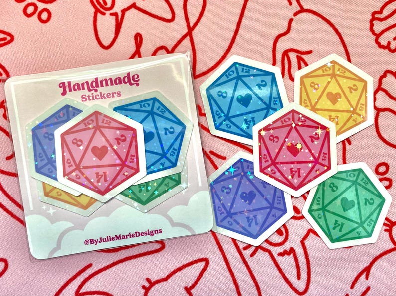 Pode incluir: Um conjunto de seis adesivos feitos &agrave; m&atilde;o com dados coloridos e brilhantes com cora&ccedil;&otilde;es no centro. Os adesivos est&atilde;o em um fundo branco com o texto "Handmade Stickers" e "@ByJulieMarieDesigns".
