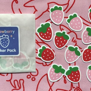 May include: A pack of strawberry stickers with a blue background and the text "Strawberry Sticker Pack". The stickers are on a pink background with red and white lines.