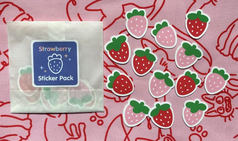 May include: A pack of strawberry stickers with a blue background and the text "Strawberry Sticker Pack". The stickers are on a pink background with red and white lines.