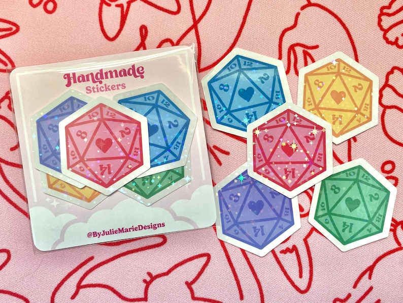 Pode incluir: Um conjunto de seis adesivos hologr&aacute;ficos iridescentes com um design em forma de cora&ccedil;&atilde;o dentro de um dado de 20 faces. Os adesivos s&atilde;o de v&aacute;rias cores, incluindo rosa, azul, amarelo, verde e roxo. Os adesivos est&atilde;o sobre um fundo branco com um design de nuvens rosa e branco. O texto "Handmade Stickers" e "@ByJulieMarieDesigns" est&aacute; impresso no fundo.