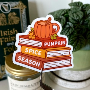 May include: A sticker with a cartoon illustration of a pumpkin spice latte on top of a stack of books. The books are labeled "Pumpkin", "Spice", and "Season".