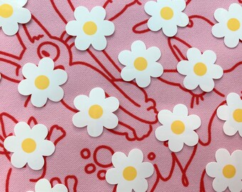 May include: A pink background with white daisy stickers with yellow centers. The daisies are scattered across the background.