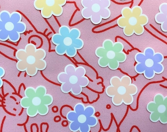 May include: A sheet of pastel colored flower stickers with white centers. The stickers are arranged in a random pattern on a pink background with red lines.
