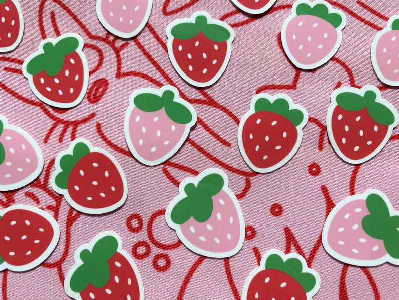May include: A collection of pink and red strawberry stickers with green leaves. The stickers are arranged on a pink background with a red line pattern.