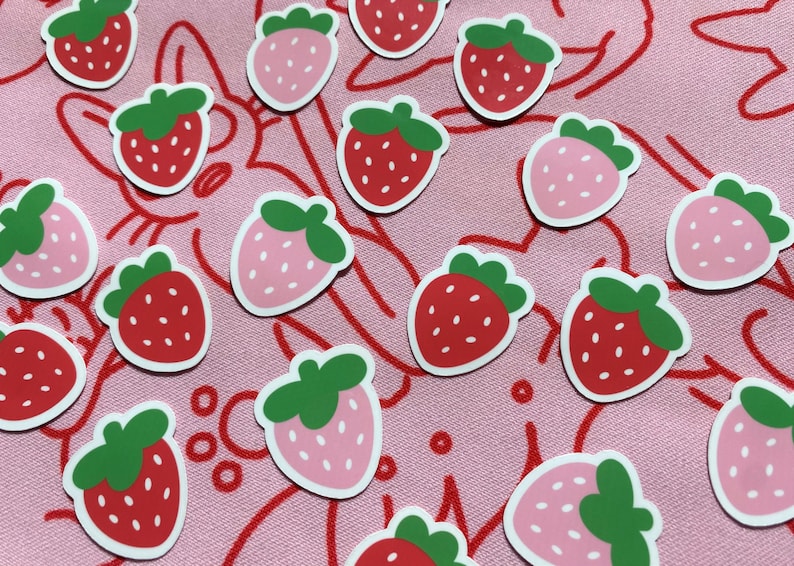 May include: A collection of red and pink strawberry stickers on a pink background. The stickers are in various positions and feature a white outline.