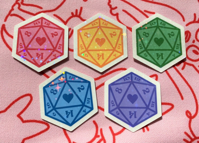 Pode incluir: Cinco adesivos coloridos de um dado de 20 faces com um cora&ccedil;&atilde;o no centro. Os dados s&atilde;o rosa, amarelo, verde, azul e roxo.