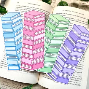 May include: Four colorful book-shaped stickers in blue, pink, green, and purple, each with white outlines. The stickers are stacked like books and are placed on an open book with text.