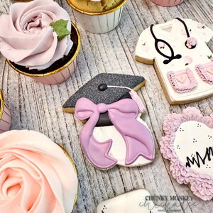 May include: A collection of decorated cookies for a graduation party. The cookies feature a graduation cap, a nurse's uniform, and a pink flower with the word "Mom" written on it.