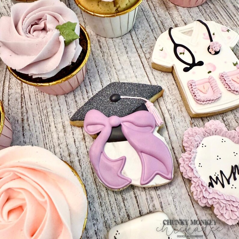 May include: A collection of decorated cookies for a graduation party. The cookies feature a graduation cap, a nurse's uniform, and a pink flower with the word "Mom" written on it.