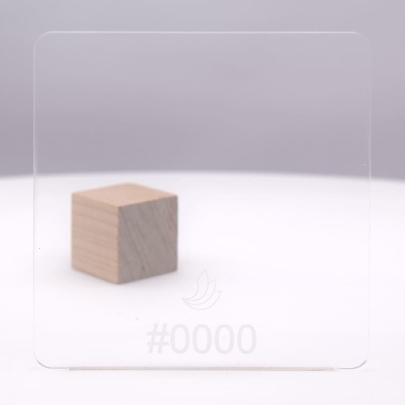 May include: A clear acrylic sheet with a white logo and the text #0000. A small wooden block is in front of the sheet.