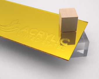 May include: A sheet of gold mirror acrylic with the text "Acrylic United States" embossed on the surface. A small wooden block is sitting on the sheet.