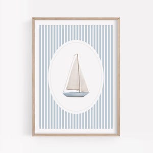 Può includere: Una stampa incorniciata con un'illustrazione ad acquerello di una barca a vela. La barca è azzurra con una vela bianca, su uno sfondo a righe azzurre chiare e medie. L'opera d'arte è racchiusa in un ovale bianco e incorniciata in legno chiaro.