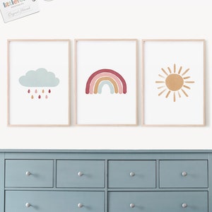 Puede incluir: Tres impresiones enmarcadas con un dise&ntilde;o minimalista. La primera impresi&oacute;n presenta una nube azul con gotas de lluvia, la segunda impresi&oacute;n presenta un arco&iacute;ris con rayas rojas, naranjas, amarillas, verdes, azules y moradas, y la tercera impresi&oacute;n presenta un sol amarillo con rayos naranjas.