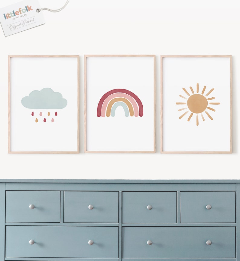 Puede incluir: Tres impresiones enmarcadas con un dise&ntilde;o minimalista. La primera impresi&oacute;n presenta una nube azul con gotas de lluvia, la segunda impresi&oacute;n presenta un arco&iacute;ris con rayas rojas, naranjas, amarillas, verdes, azules y moradas, y la tercera impresi&oacute;n presenta un sol amarillo con rayos naranjas.