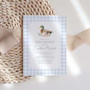 May include: A blue and white gingham baby shower invitation with a watercolor illustration of a duck. The invitation text reads "Kindly join us for a Baby Shower in honor of Caroline Michaels. Saturday, August 21, 2014, 2 o'clock in the afternoon, Westview Country Club, 432 Henderson Dr. Aubrey, TX 76543. Kindly RSVP by September 1st, Text Jocelyn at 321.4567, Registered at Baby Boutique."