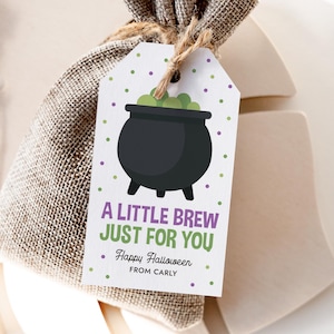 Könnte beinhalten: Ein weißes, rechteckiges Geschenkanhänger-Etikett mit einer schwarzen Kesselgrafik, gefüllt mit grünen Blasen, lila und grünen Punkten sowie dem Text A LITTLE BREW JUST FOR YOU, Happy Halloween, FROM CARLY, befestigt an einem Jutebeutel mit Kordel.